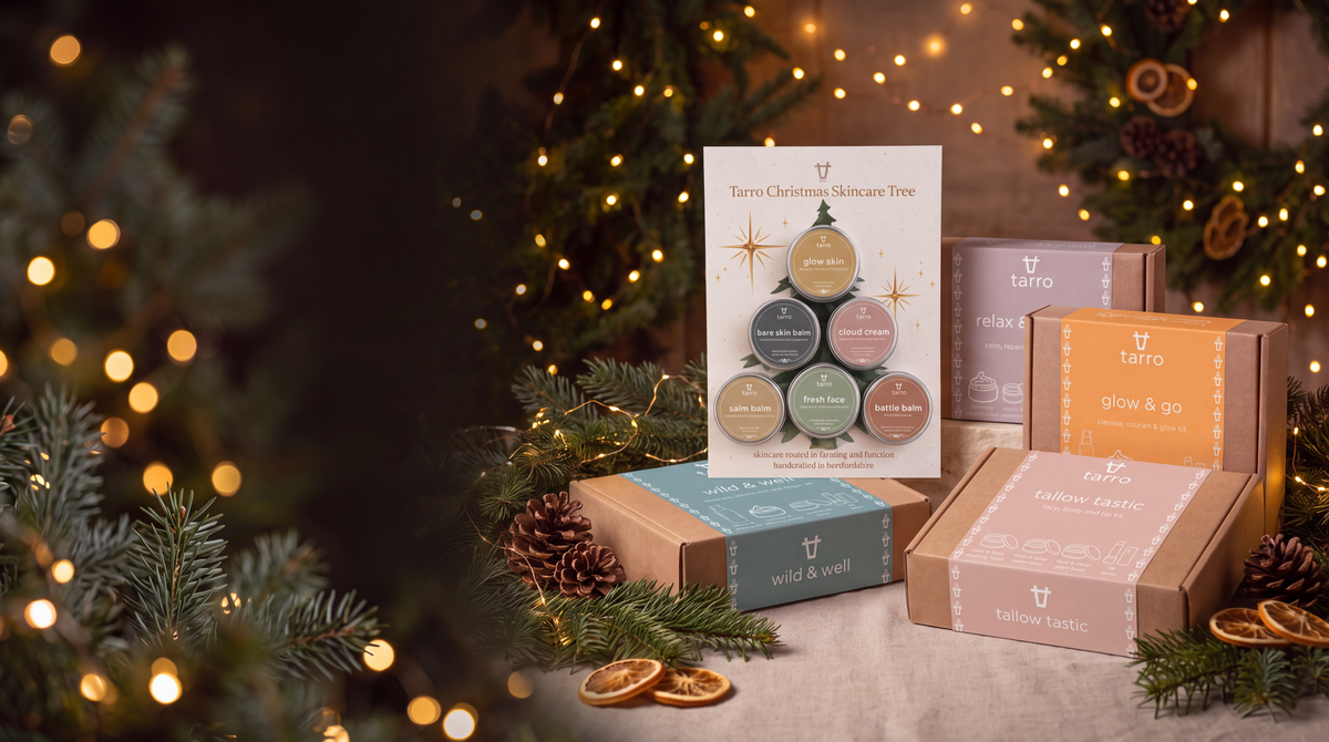 A curated holiday gift set from Tarro, featuring a 'Tarro Christmas Skincare Tree' gift set booklet and several gift boxes in kraft paper and colored packaging, styled on a table with pine branches, dried orange slices, and warm Christmas lights in the background.